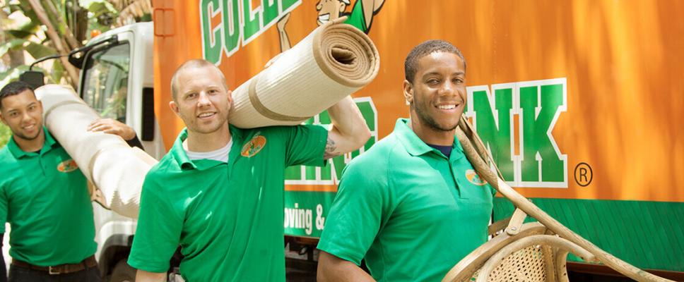 Three men in front of a moving truck, holding furniture.